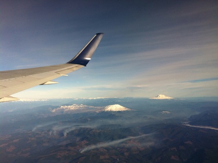 The plane flying in the blue sky above mountain, lake, and snow fieldの素材