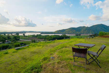View photos of brown chairs and tables laid on the green lawns on the high mountains in the evening. There is the Mekong River in front and a village in a rural area. Feeling relaxed and calm.の写真素材