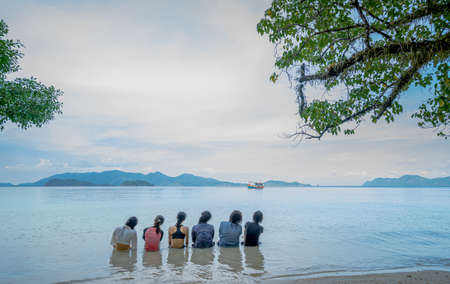 Photos from the back of a group of women sitting on the beachside. There is a boat sailing in the middle of the sea. The ocean is clear blue water, clean and quiet. Feeling love and happiness.の写真素材