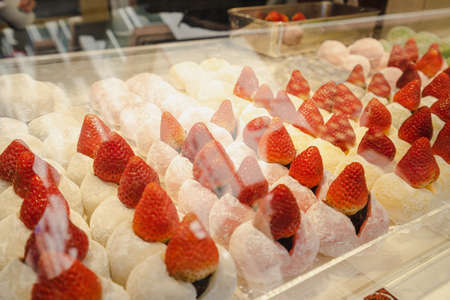 A shot through the glass of various flavors of Daifuku with fresh strawberries inserted in the center. They are arranged neatly in a row, separated by color on a plastic shelf. Feeling delicious.の写真素材
