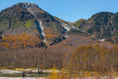 Photos from the back of women standing by the river in Kamikochi, Japan. There are many colorful trees in autumn. Idea of traveling with friend backgrounds. There is a copy space on the right and top.の写真素材