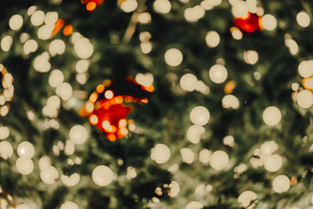 Blurred background of Christmas trees with yellow lights and colorful balls at night. There is much circular bokeh with warm tones. Feeling happy. The idea for celebration wallpaper with copy space.の写真素材