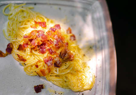 Top view of a white plate carbonara cheese. the yellow color of spaghetti contrasts with the red color of the bacon, making it look appetizing and vibrant. Concept of home cooking with family.の写真素材