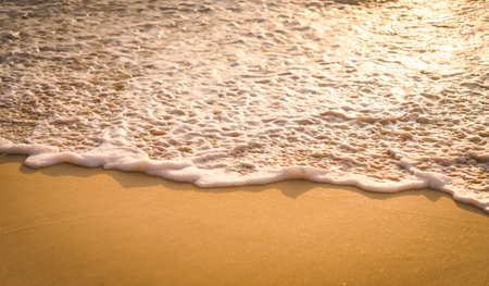 Sea waves hit the coast causing white bubbles and splashes of water. The orange color glow of the sunset creates warm tones. Fine sandy beaches with glistening. Feeling relaxed and refreshed.の写真素材