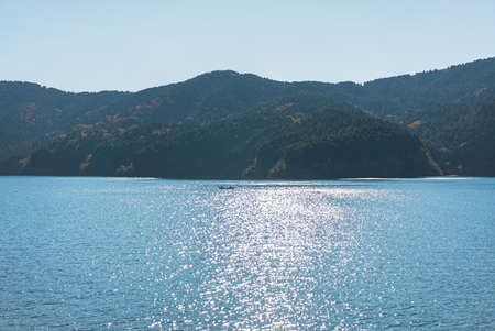 Photos from the boat on the ocean in the morning, sunlight shines on the water as glistening light. Blue sky has streaks of clean white clouds. there is an island full of green trees in the back.の写真素材