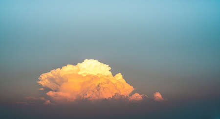 A photograph of a large golden-yellow cloud in the twilight colored sky in the evening. Its edges are wavy and fluffy with a soft blue backdrop. Feeling calm and relax. There is a copy space on top.の写真素材