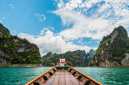 View from a wooden Thai style boat in dam with emerald water and white big stonds. There are many limestones, clear blue sky. Feeling fresh and relax. Ideas for traveling background with copy space.の写真素材