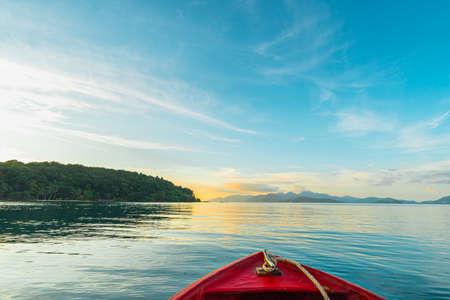 View from a red boat in the indigo ocean in the evening with golden light. There are many islands and a clear blue sky. Feeling fresh and relax. Ideas for traveling background with copy space.の写真素材