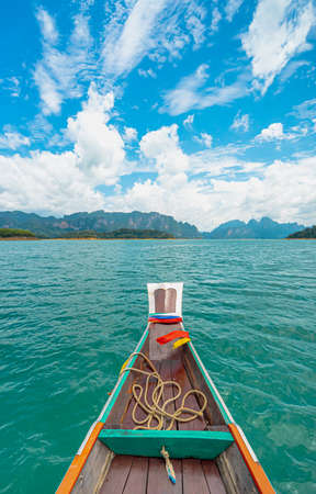 View from a wooden Thai style boat in dam with emerald water and white big stonds. There are many limestones, clear blue sky. Feeling fresh and relax. Ideas for traveling background with copy space.の写真素材