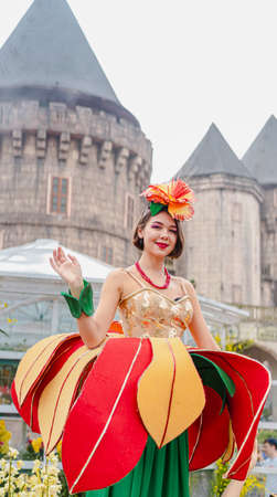 DA NANG, VIETNAM - March 25, 2019: An unknown foreign woman with short brown hair in a colorful fantasy floral dress poses with a smile for tourists on Bana Hill. There is a light brown castle behind.のeditorial素材