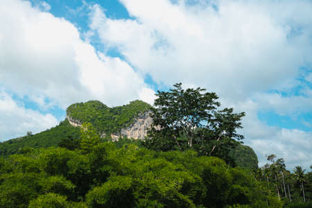 Landscape photo of heart shape rocky mountain with clear blue sky and white fluffy clouds. There are many trees around with lush green color. The idea for exotic natural wallpaper with copy space.の写真素材