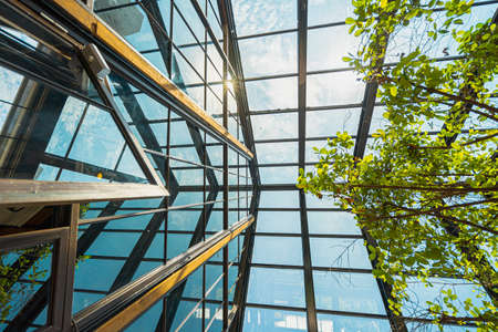 PHUKET, THAILAND - 20 MAY 2020: Low angle shot of mirrored roof with a view of the sky, white clouds, and light-reflecting. There is a transparent structure with steel and the wall is clear glass.のeditorial素材