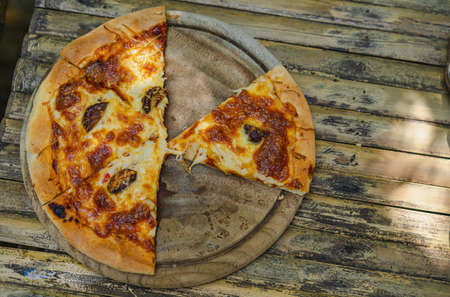 Close-up shot of a mushroom pizza that has been divided into pieces placed on a simple wooden tray. It was baked until yellowed to brown on a pale old bamboo table. Feeling of hunger and delicious.の写真素材