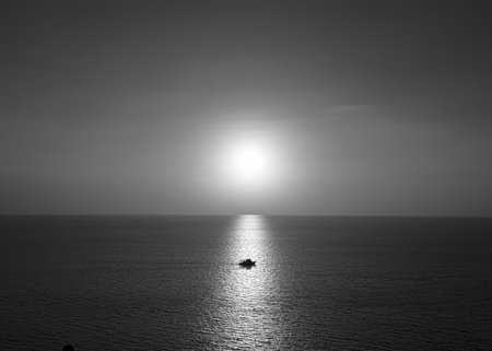 Photos of the boat on the ocean in the evening. Sunshine on water as glistening light with black and white color.  There is a horizon line behind. The idea for monochrome background with copy space.の写真素材