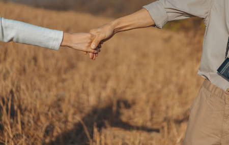 Woman and man holding hands on a golden yellow meadow. Backdrop are shadows of both of them on the ground. Feelings of love and romance. Ideas for Valentine's Day wallpaper with copy space.の写真素材