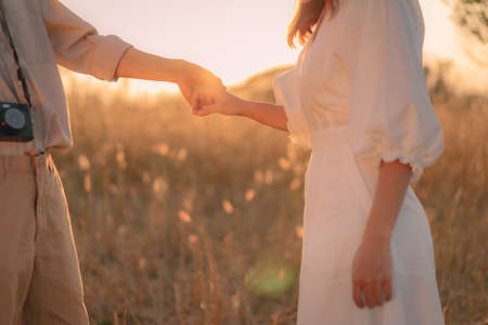 Woman and man holding hands on a golden yellow meadow. There was an orange evening light shining down on both of them in soft tones. Feelings of love and romance. Ideas for Valentine's Day wallpaper.の写真素材