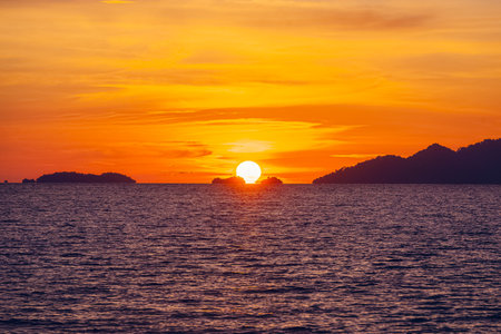 A front view of the sunset over the ocean with an orange and yellow. There are many islands behind. There is golden light reflecting off the water. The idea for natural wallpaper with copy space.の写真素材