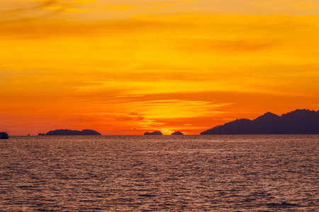 A front view of the sunset over the ocean with an orange and yellow. There are many islands behind. There is golden light reflecting off the water. The idea for natural wallpaper with copy space.の写真素材