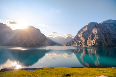 The front view of Tientang Hu lake, Xinjiang, China. There are many layers of mountains in the background. The sun was rising with yellow light reflected on the water. The idea for Trekking wallpaper.の写真素材