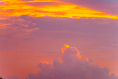 A photograph of a large golden-yellow cloud in the twilight colored sky in the evening. Its edges are wavy and fluffy with a soft blue backdrop. Feeling calm and relax. There is a copy space on top.の写真素材