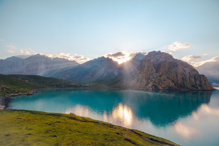 The front view of Tientang Hu lake, Xinjiang, China. There are many layers of mountains in the background. The sun was rising with yellow light reflected on the water. The idea for Trekking wallpaper.の写真素材
