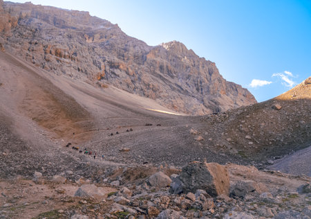 High-angle view of the Tianshan Mountains with steep, rocky hills on sunny days. Many hikers and horses are seen walking in the distance. Idea for adventure activities background with copy space.の写真素材
