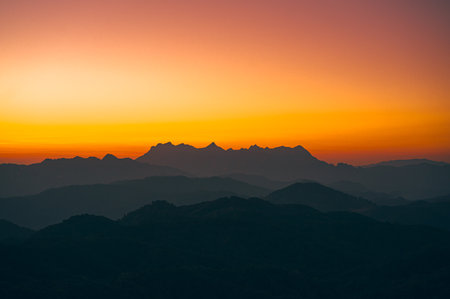 High-angle view of a beautiful orange, pink, and yellow sky in the evening as the sun sets. There is a view of a mountain in the center of the image, which has a unique shape.の写真素材