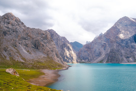This is a morning view of the campsite on a cloudy day at Tian Tang Hu Lake, Xinjiang, China. A green lawn is surrounded by blue water and many limestone mountains. The idea for landscape wallpaper.の写真素材