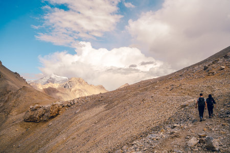 Wide-angle shot of a couple of hikers walking on a steep rocky slope in the Tianshan Mountains in Xinjiang, China. Midday sunlight streams down on the peaks on a clear day with space for copying.の写真素材