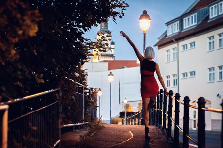 Beautiful young woman in a red dress standing on the street in the evening.の写真素材
