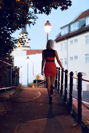 Blonde girl in a short red dress runs along the embankment of the old town.の写真素材