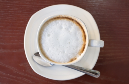 Hot cappuccino coffee in white cup with spoon on wood table の写真素材