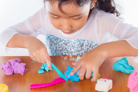 Little girl is learning to use colorful play dough on white backgroundの写真素材