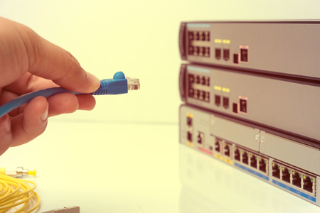 Close-up Hand holding ethernet cable on network switches background.Hand holding RJ45 Connectors on UTP cable, selective focus, filtered warm tone color.の写真素材