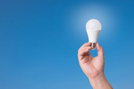 Hand holding LED Bulb with Lighting on blue sky background. Eco power concept.の写真素材