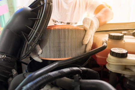 auto mechanic wearing protective work gloves holding a dirty, air filter over a car engine for cleaningの写真素材