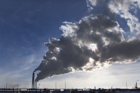 Smoking chimney at sunset on industrial buildings complex.