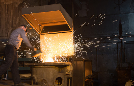 Hard work in the foundry, worker controlling iron smelting in furnaces. Sparks.