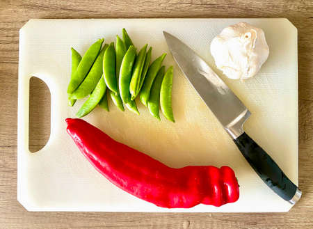 Sweet red Ramiro pointed pepper and sugar snap peas on a chopping boardの写真素材