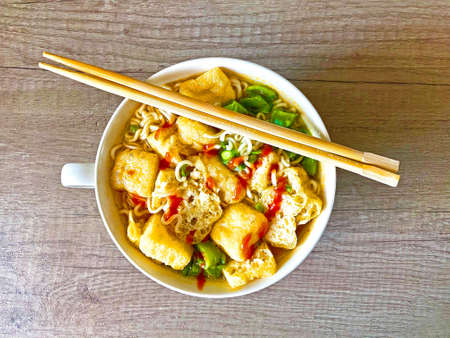 Bowl of delicious deep fried Tofu in an Asian spicy seafood and chicken broth with noodles and chilliの写真素材