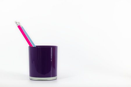 A violet glass desktop organizer on a white backdrop contains three pencils with erasers in pink, blue, and navy hues.の写真素材