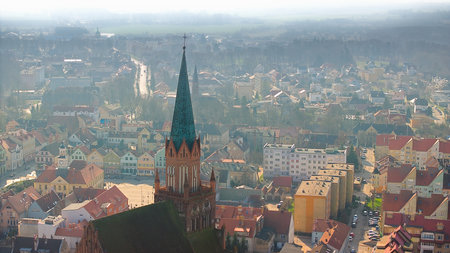 Aerial view of TrzebiatÃ³w on a gray day, with the 90m Gothic church spire commanding the skyline. The red-brick tower overlooks varied buildings and expansive greenery.の写真素材