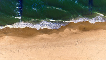 Peaceful Baltic Sea texture seen from above - soft golden tones of sand meeting the shimmering blue water under clear, sunny March skies.の写真素材