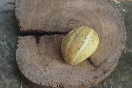 A vibrant green melon rests on a rustic wooden board, showcasing natural textures and earthy tones. Ideal for themes of healthy eating and summer freshness.の素材