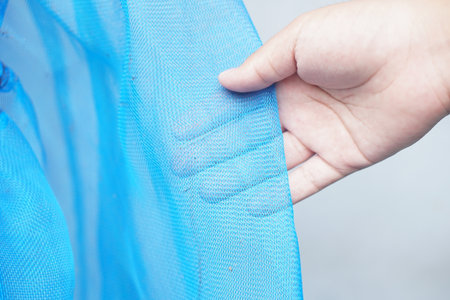 A close-up image of a hand gently touching a soft blue mesh fabric, highlighting the delicate texture and transparency, perfect for fashion or design projects.の素材