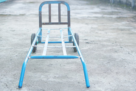 A simple blue metal trolley rests on a concrete surface, designed for versatile transportation and storage needs in both industrial and everyday settings.の素材