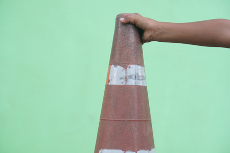 A person holds a traffic cone against a vibrant green background, highlighting the importance of safety in urban settings while drawing attention to design details.の素材