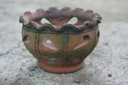 Stunning clay pot with intricate cutout details resting on a weathered surface, showcasing traditional craftsmanship and rustic charm for home and garden decor.の素材