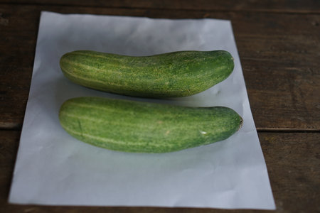 Fresh green cucumbers resting on a white sheet of paper create a striking visual on rustic wood, perfect for healthy food concepts and culinary inspirations.の素材