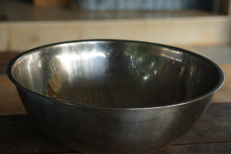 A polished metal bowl rests gracefully on a rustic wooden table, showcasing its reflective surface against a softly blurred background, perfect for kitchen settings.の素材